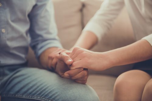 A woman holding a man's hand and touching his arm.