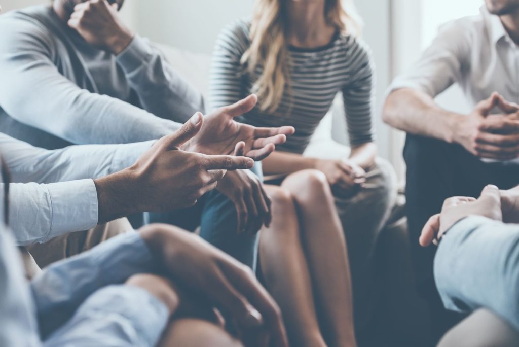 A group of adults sitting in a circle while a person shares their story in group therapy